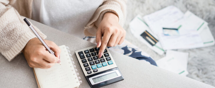 woman writing a list of debt on notebook calculating her expenses with calculator with many invoices , female hand doing accounting