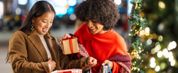 Two female friends are enjoying the christmas spirit by giving each other presents in a beautifully decorated city street